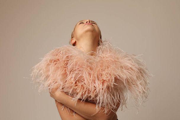 Indoor portrait of beautiful blond young woman wearing pink marabou feathers. High quality photo. - Zdjęcie, obraz