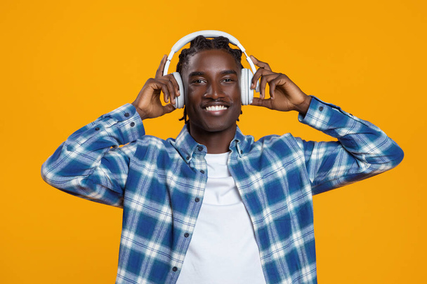 Портрет щасливого молодого чорного хіпстера Хлопця Прослуховування музики в бездротових навушниках, Веселий тисячолітній афроамериканський чоловік насолоджується улюбленими піснями і посміхається на камеру, позуючи над жовтим тлом - Фото, зображення