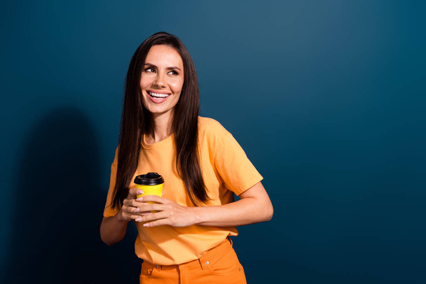 Photo of lady in t shirt holding yellow paper cup latte macchiato looking empty space ad coffee shop isolated on dark blue color background. - Foto, Bild