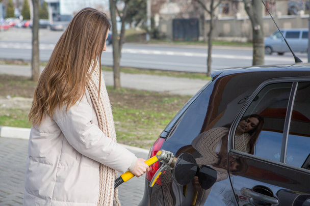 Nuori nainen pitelee polttoainesuutinta kädessään tankatessaan autoa huoltoasemalla. Polttoainetankkaus bensa-asemalla. Auton tankkaaminen kaasulla. - Valokuva, kuva