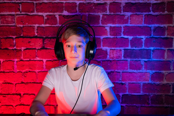 Bawi się nastolatek. Chłopak gracz gra w gry komputerowe przeciwko neonowej ścianie z cegły. - Zdjęcie, obraz