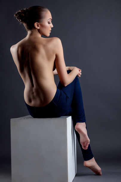 Topless model posing sitting on cube. Back view - Foto, afbeelding
