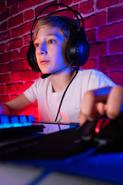 Un appassionato compagno di gioco di fronte a un computer. Un ragazzo giocatore gioca ai giochi per computer contro un muro di mattoni illuminato al neon. - Foto, immagini