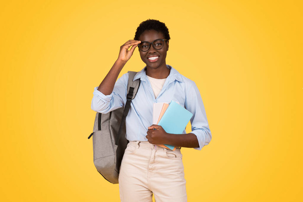 Egy tudós fekete nő tanuló szemüveggel, mélyen elmerülve a könyvek olvasásában, összpontosított viselkedése és intellektuális kíváncsisága élénken megragadta a világos sárga háttér - Fotó, kép