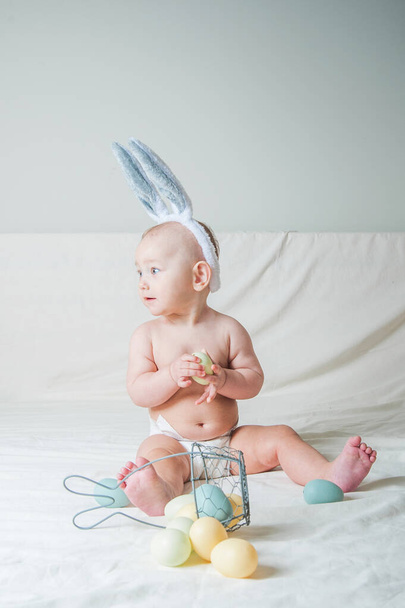 Κοριτσάκι 1 έτους στο κρεβάτι με καλάθι και πασχαλινά αυγά. Κυνήγι αυγών, παιδική δραστηριότητα. - Φωτογραφία, εικόνα
