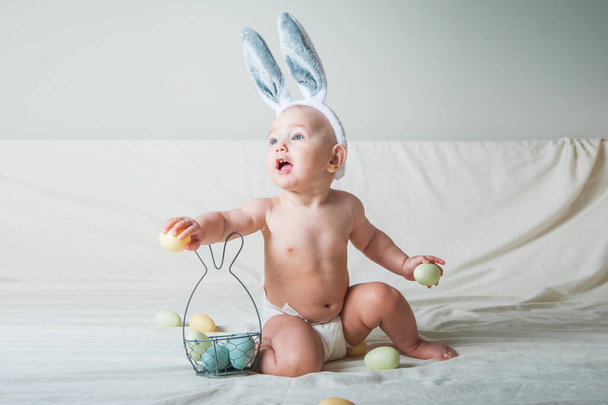 Niña de 1 año en la cama con cesta y huevos de Pascua. Caza de huevos, actividad infantil. - Foto, imagen