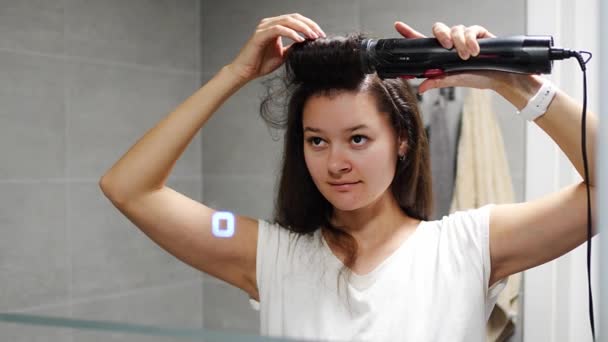 Nuori nainen tuulet kiharat harjalla kiinnitys käyttäen multi-styler hiustenkuivaaja kotona kylpyhuone. Käsite hiustenhoito, muoti ja kauneus. Heijastunut näkymä peilistä. Laadukas 4k kuvamateriaalia - Materiaali, video