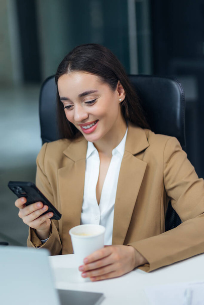 Happy young inspired caucasian business woman looking at mobile phone screen, reading email with good news, enjoying studying or working distantly on online project at modern home office. - Photo, Image