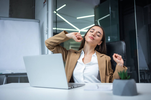 Relaxált irodai munkás nő nyújtja a kezét és a testét, szünetelteti a munkát a laptopon. Örömteli szabadúszó szövegíró lány elégedett a munkahelyi feladattal coworking térben - Fotó, kép