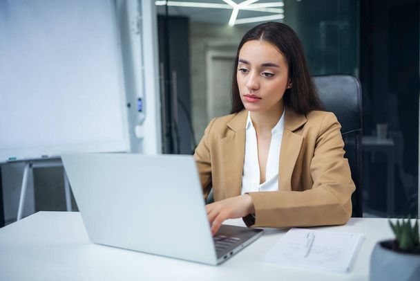 Znudzony niemotywowana kobieta pracownik siedzi w biurze z laptopem wykonując monotonną pracę lub nieciekawe zadanie. - Zdjęcie, obraz