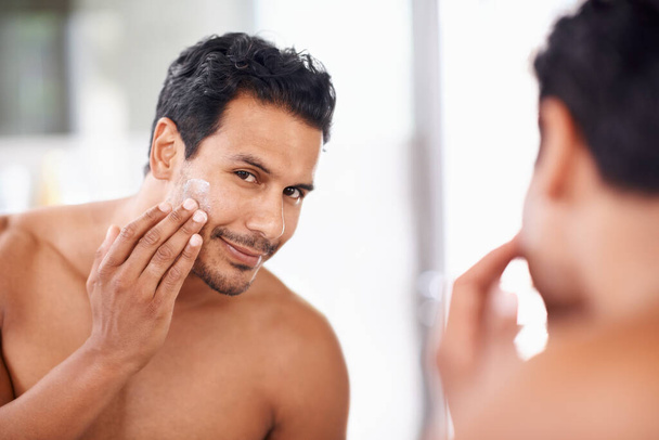 Skincare, mirror and cream with man in bathroom for morning routine, facial treatment and cosmetics. Self care, confidence and face of male person for sunscreen, lotion or moisturizer in reflection - Photo, Image