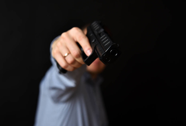 Un hombre sosteniendo un arma negra en su mano. Apuntando la pistola. Fondo negro.  - Foto, Imagen