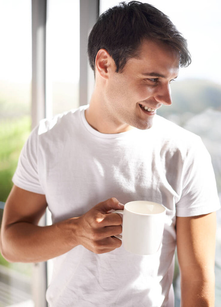 Mies, muki ja hymy kahvi ikkunalla makuuhuoneessa, huoneistossa ja hotellihuoneessa aamulla, herääminen ja uusi päivä. Mies henkilö, aikuinen ja onnea teetä, espresso ja cappuccino Espanjassa. - Valokuva, kuva