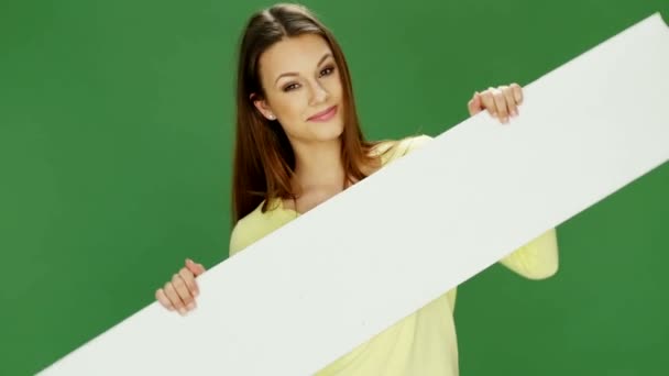 Atraktivní mladá žena držící bílý nápis na zeleném pozadí - Záběry, video
