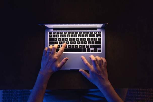Man is typen gebruik laptopcomputer werken bij donkere nacht. Schrijver plat leggen bovenaanzicht werkplek. - Foto, afbeelding