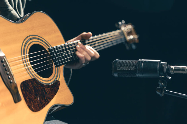 Мужчина-музыкант играет на акустической гитаре за микрофоном в студии звукозаписи. Концепция записи, репетиции или живого исполнения музыки. - Фото, изображение