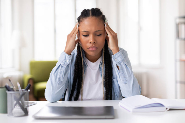 Zaostřená černošky teen studentka s copánky pocit stresu při studiu na notebooku, dotýkání chrámů, sedí v světlé domácí kanceláři nastavení - Fotografie, Obrázek