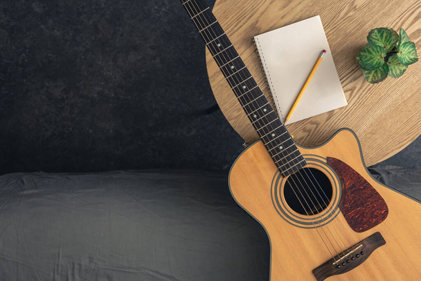 テーブルの上に鉛筆が付いている音響ギターおよびノートのパッド,上の眺め. 音楽的背景,リハーサルの概念,ギターを演奏することを学ぶ. コピースペース. - 写真・画像