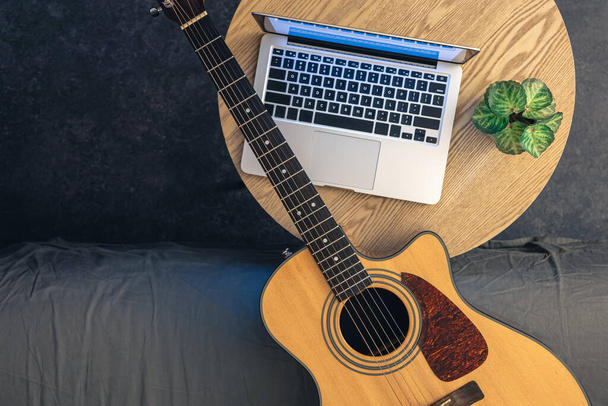 Ακουστική κιθάρα και laptop σε ξύλινο τραπέζι, πάνω όψη. Μουσική και τεχνολογία, ψηφιακή έννοια. Online μαθήματα κιθάρας. - Φωτογραφία, εικόνα