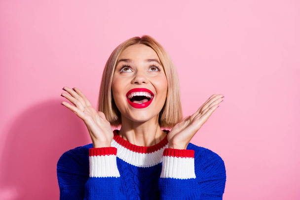 Photo of attractive young blonde bob hair girl wear blue sweater touch cheeks looking up empty space isolated on pink color background. - Fotó, kép