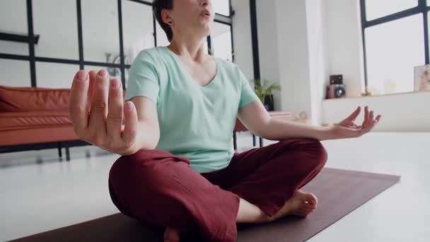 Concept of a pleasant and useful pastime in old age. Old woman make yoga exercise at home. Mature woman have meditation. She look at camera and smile. High quality 4k footage - Footage, Video
