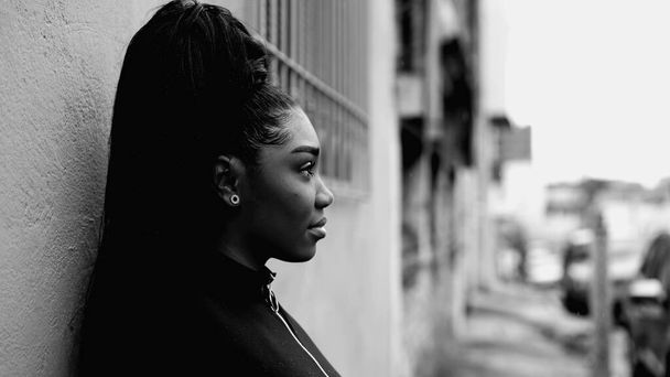 Monokromatikus portré a nyugodt afro-amerikai nőről - meditatív pillantás a városi esőben és támaszkodás az utcai falra, fekete-fehér - Fotó, kép