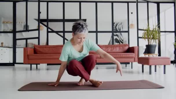 Oude vrouw doet thuis yoga-oefeningen. Volwassen vrouw hebben meditatie. Ze gaat op het bed zitten, kijkt uit het raam en is blij dat ze tijd heeft om te rusten. Hoge kwaliteit 4k beeldmateriaal - Video