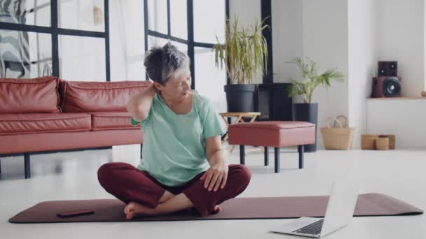 Oude vrouw doet thuis yoga-oefeningen. Volwassen vrouw bereidt zich voor om te oefenen door het opwarmen van spieren, nek, handen, hoofd. Hoge kwaliteit 4k beeldmateriaal - Video
