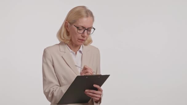 Egy nő formális ruhában és szemüvegben ül, kezében egy írótáblával, és ráír. A szemüvege javítja a látását, míg az ingujja gesztusait a szemfehérje betűjével. Egy rendezvényen van. - Felvétel, videó