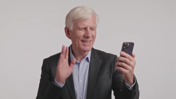 Een oudere man in formele kleding gebruikt een mobiele telefoon op een evenement. Hij gebaart met zijn duim terwijl hij in de microfoon van de gadget praat, en deelt audio met het communicatieapparaat - Video