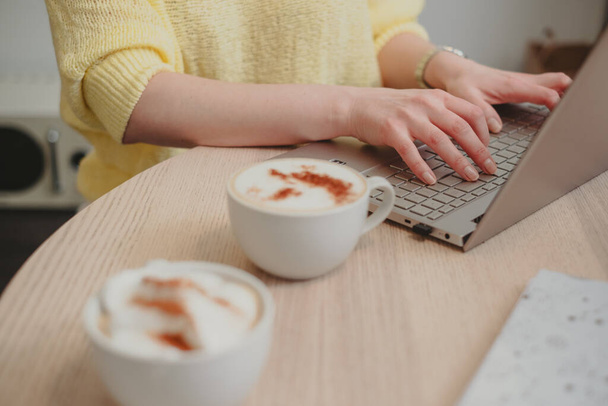Крупный план на руках, печатающих на ноутбуке, рядом с пенящимися капучино, кофе, предполагающий продуктивный кофе-брейк, деловой и личностный рост. Высокое качество фото - Фото, изображение