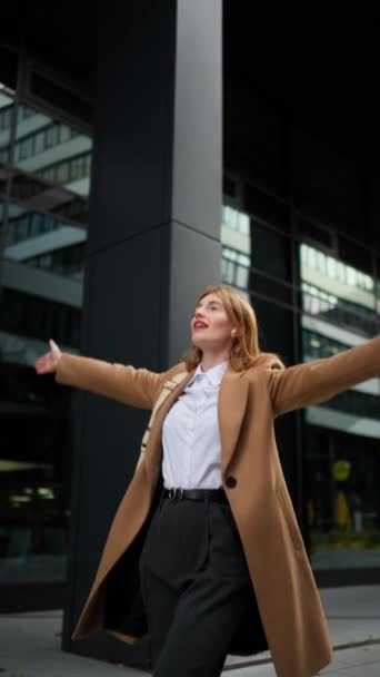 Vista vertical de la mujer feliz bailando al aire libre contra el edificio de oficinas. Entusiasta empresaria motivada celebrando la victoria bailando fuera del centro de negocios - Imágenes, Vídeo