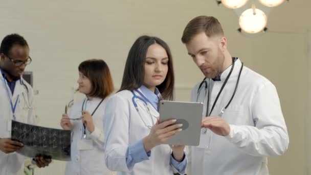 Grupa lekarzy rozmawiających o przyszłej operacji, patrzących na tablet, badających dane na zdjęciu rentgenowskim - Materiał filmowy, wideo
