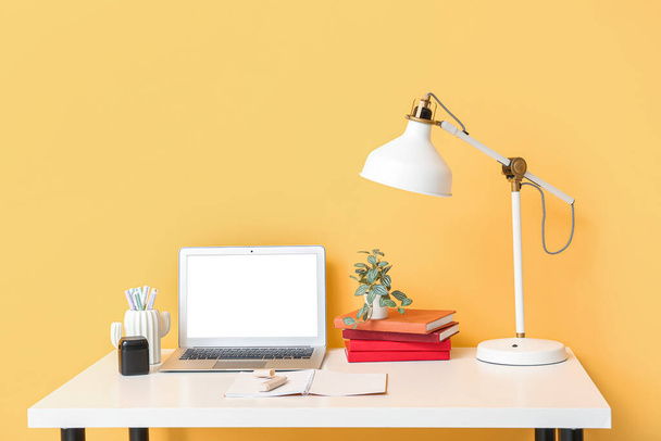 Komfortowe biuro domowe z laptopem, lampą i książkami na stole w pobliżu kolorowych ścian - Zdjęcie, obraz
