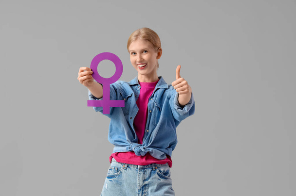 Young woman with gender symbol showing thumb-up on light background - Photo, Image
