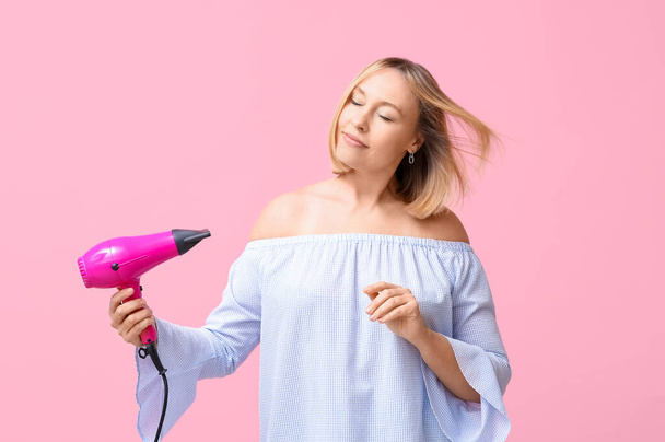 Hermosa mujer joven con peinado bob celebración secador de pelo sobre fondo rosa - Foto, Imagen
