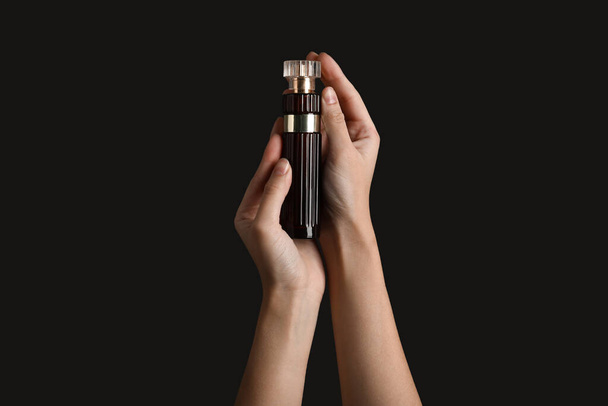 Manos femeninas sosteniendo frasco de perfume sobre fondo negro - Foto, Imagen