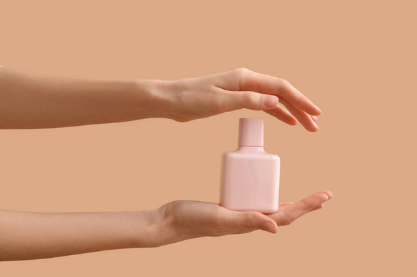 Manos femeninas sosteniendo botella de perfume rosa sobre fondo de color - Foto, imagen
