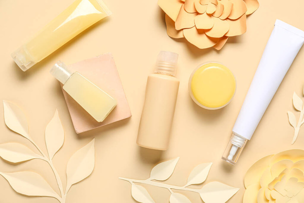 Flessen cosmetische crème met papieren bloemen en bladeren op beige achtergrond - Foto, afbeelding