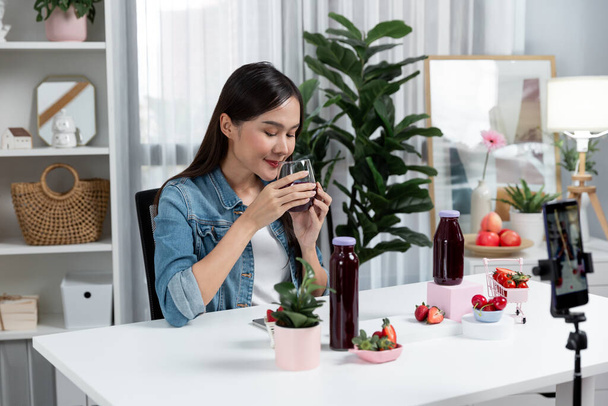Lächelnde junge schöne Asiatin, die leckere Erdbeer- und Kirschsaft-Entgiftungsgetränke testet und ein gesundes Produkt zeigt, um in den sozialen Medien Werbung für Sonderaktionen zu machen. Stratagem. - Foto, Bild