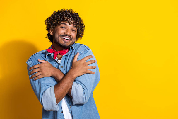 Photo portrait of attractive young man hugging self care dressed stylish denim clothes red scarf isolated on yellow color background. - Φωτογραφία, εικόνα