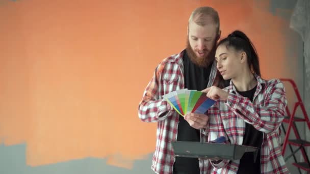 Νεαρό ζευγάρι συζητά την ανακαίνιση ενός σπιτιού επιλέγοντας χρώμα με χρωματική παλέτα. Αντιγραφή χώρου - Πλάνα, βίντεο