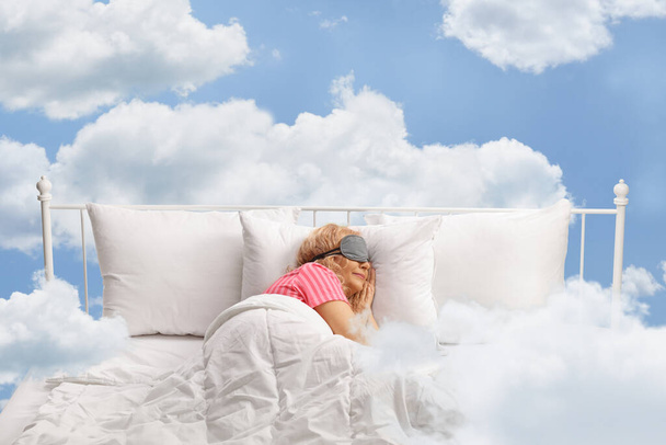 Woman sleeping with a mask and floating on clouds in the sky - Foto, afbeelding