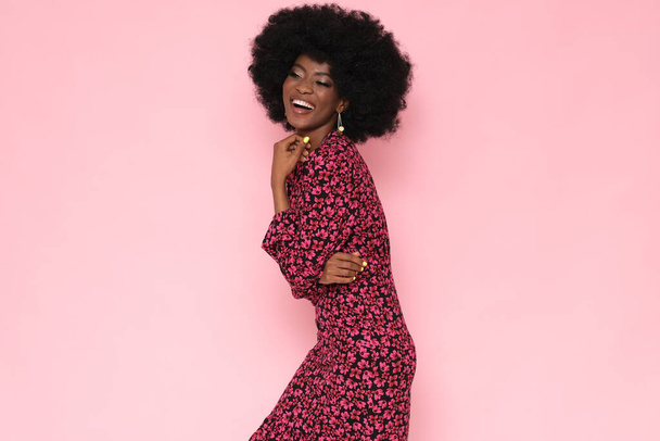 Hübsche schwarze Frau in einem floralen Kleid auf rosa Hintergrund. - Foto, Bild