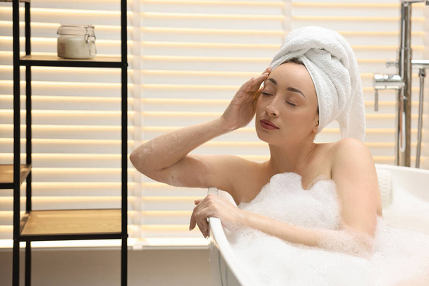Beautiful woman taking bath with foam in tub indoors - Fotó, kép