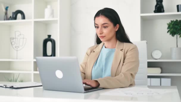 Elegante succesvolle Indiase of Arabische zakenvrouw, bedrijfsmedewerker die op kantoor zit, laptop gebruikt, aan een project werkt, naar de camera kijkt, vriendelijk glimlacht - Video