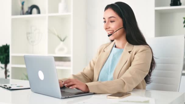Video consultation. Successful positive arabian or indian young woman, call center operator with headset, working on support help desk in the office with a laptop, smiling. Customer support service - Footage, Video
