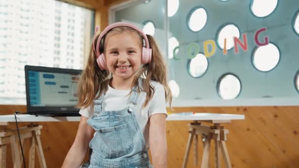 Little pretty caucasian girl smiling to camera while showing a thumb up gesture. Young child wearing headphone and casual dress standing while looking at camera with satisfy, happy, joyful. Erudition. - Footage, Video