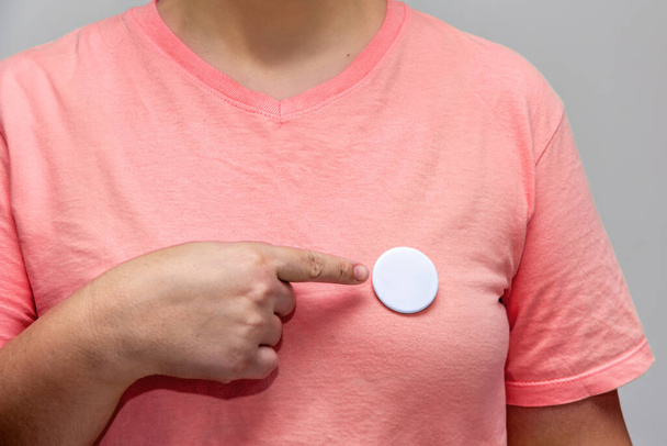 Жінка в рожевій сорочці вказує на блискучу круглу кнопку. Ізольований макет значка штифта - Фото, зображення