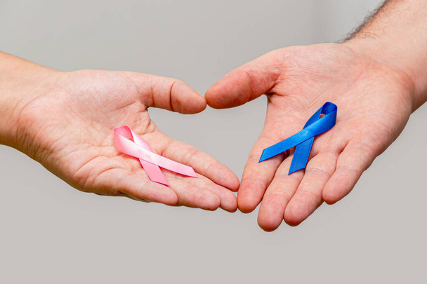 Zwei Hände mit zwei rosa und blauen Bändern für die Kampagnen Rosa Oktober und Blauer November zur Unterstützung des Lebens und zur Sensibilisierung für Krebs. Hand des Mannes und Hand der Frau - Foto, Bild